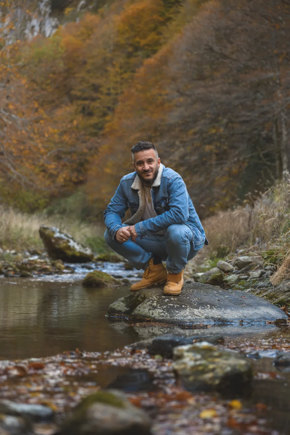 A'Rieka accroupi sur un rocher, au bord d'une rivière en automne